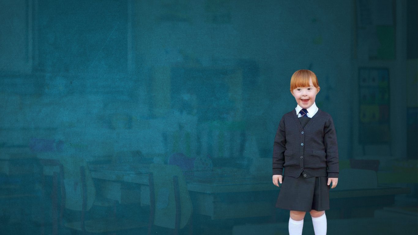 child wiht down syndrome in a primary school outfit with cardigan and skirt and high white socks and a tie. she's smiling for the photo and standing straight with her arms by her side