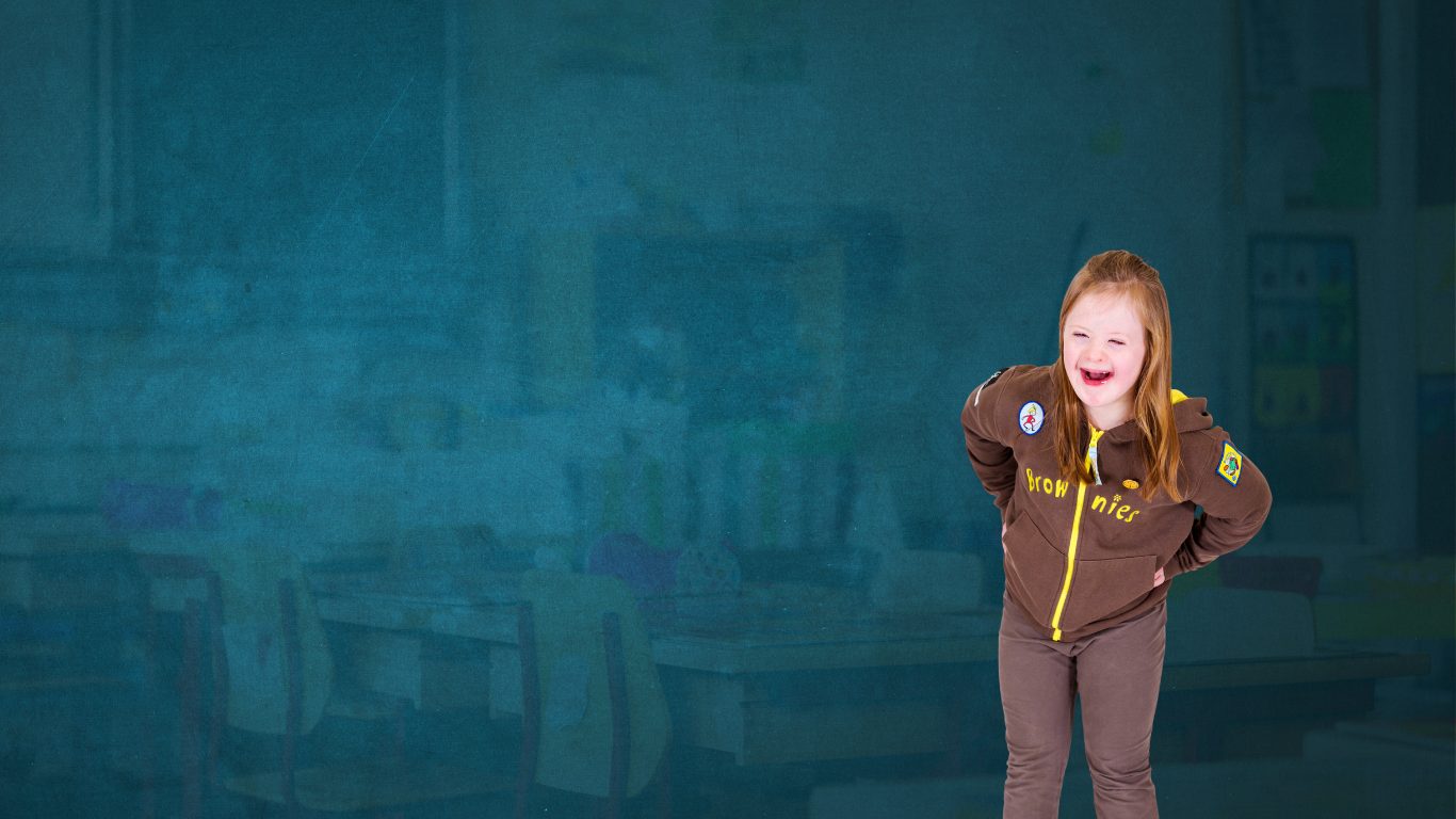 Girl with down syndrome is smiling and posing for a photo with her hands on her hips, leaning forward and wearing a brownies jumper