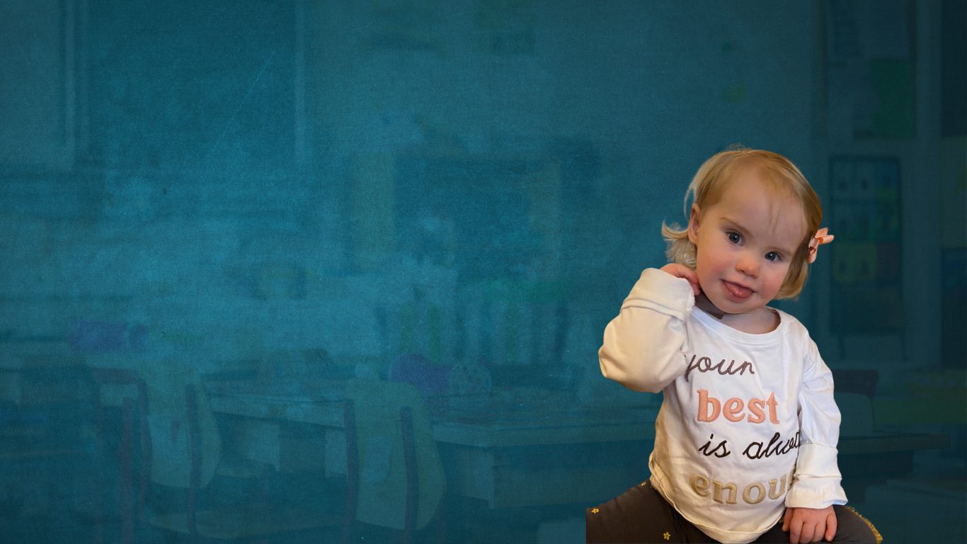 child with down syndrome posing for a pic with their tongue sticking out, the child is of toddler age