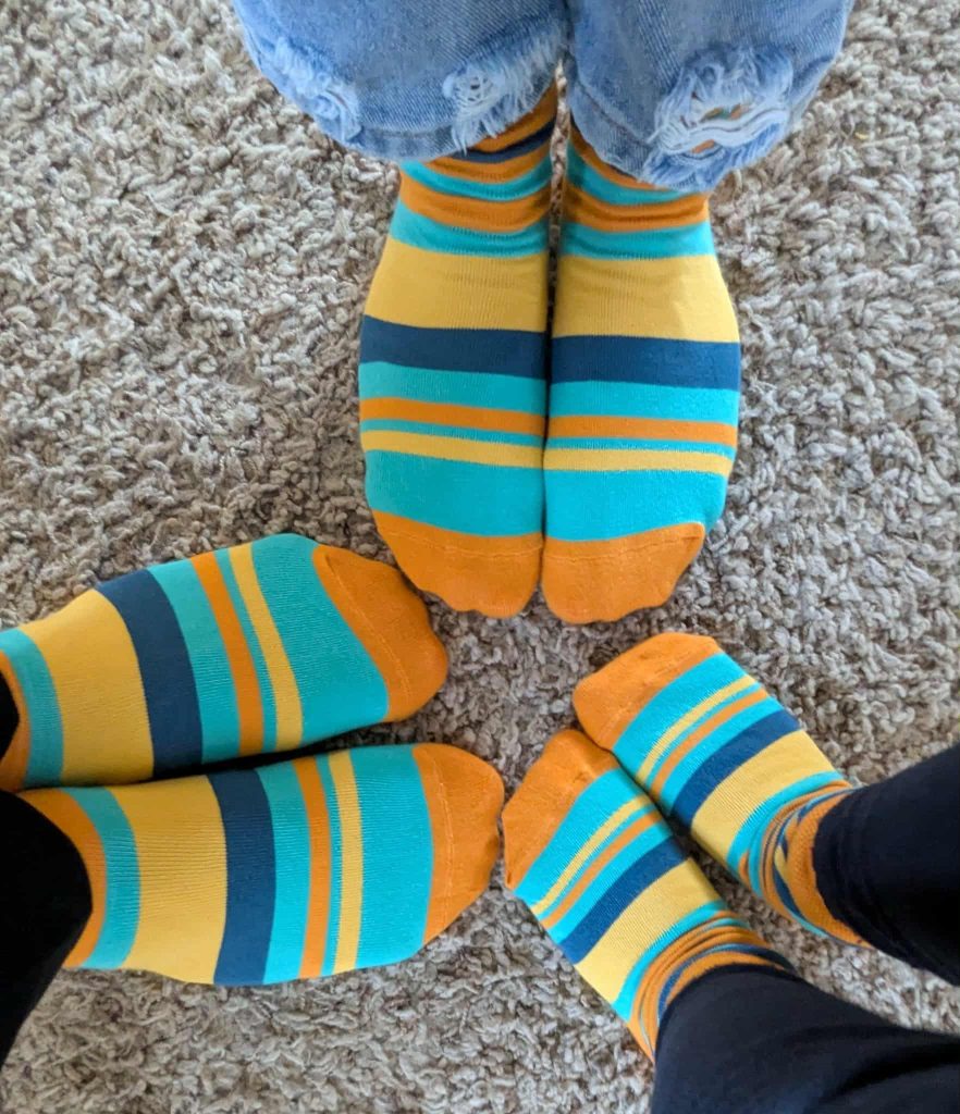 a close up of 3 pairs of feet wearing dsuk socks. the feet are pointing towards each other in a circle, you can see two adult feet and one pair of children's feet