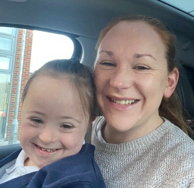 Victoria McDonnell and her daughter Ivy who has down syndrome, Vicky is hugging her daughter from behind as they both smile for a photo