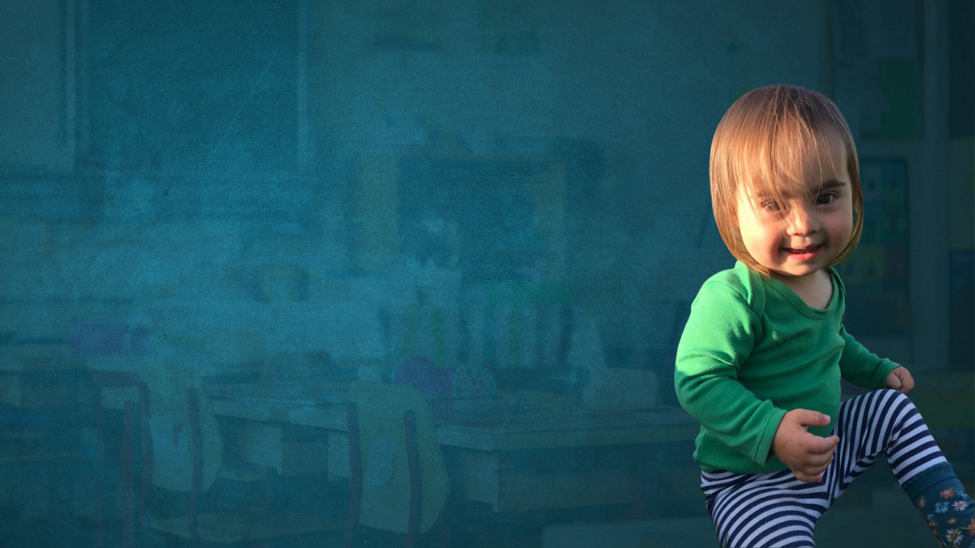 Young person with Down syndrome syndrome sitting down and smiling at the camera with his hair covering his eyes
